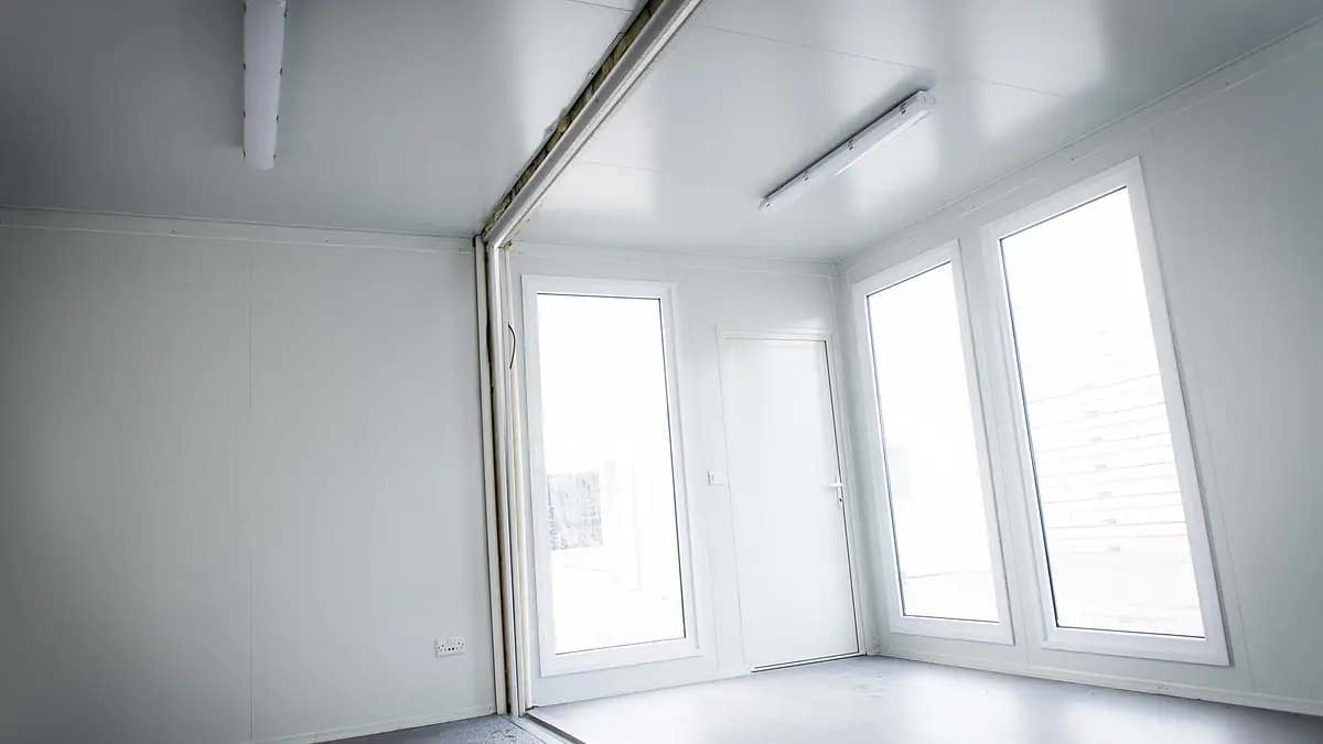 Interior of a bright modular room with white walls and large windows allowing natural light to fill the space.